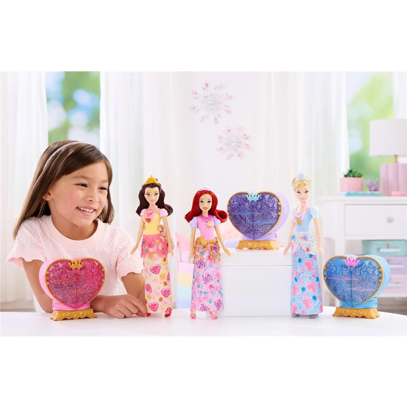A girl smiles while playing with four Disney Princess fashion dolls, including Ariel, in colorful outfits beside decorative heart-shaped displays.
