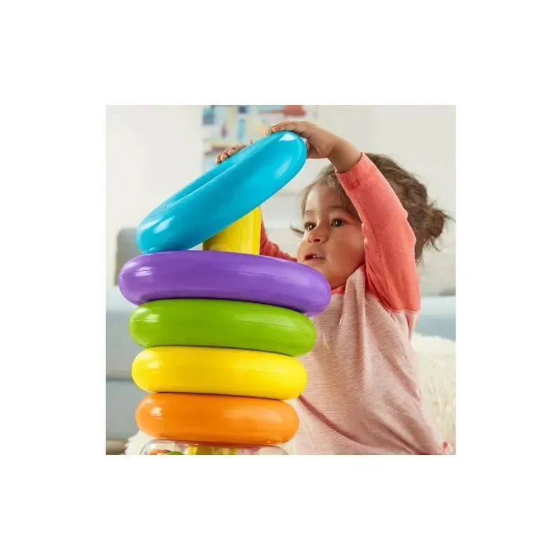 A child places a blue ring on the top of a colorful Fisher Price Giant Rock-A-Stack toy, which includes an orange base and stacked rings in green, yellow, purple, and blue.