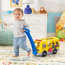 Toddler pulls a Fisher Price Little People school bus toy with colorful characters inside, promoting early learning and play.