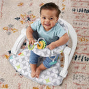 Portable baby chair with developmental toys; a smiling baby sits in a gray and white patterned seat, holding colorful rings.