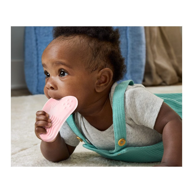 Baby lying on a soft surface, holding a pink teething toy while looking curiously at the surroundings.