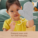 Young child wearing a colorful shirt holding a gray pretend oven mitt, engaging in imaginative cooking play.