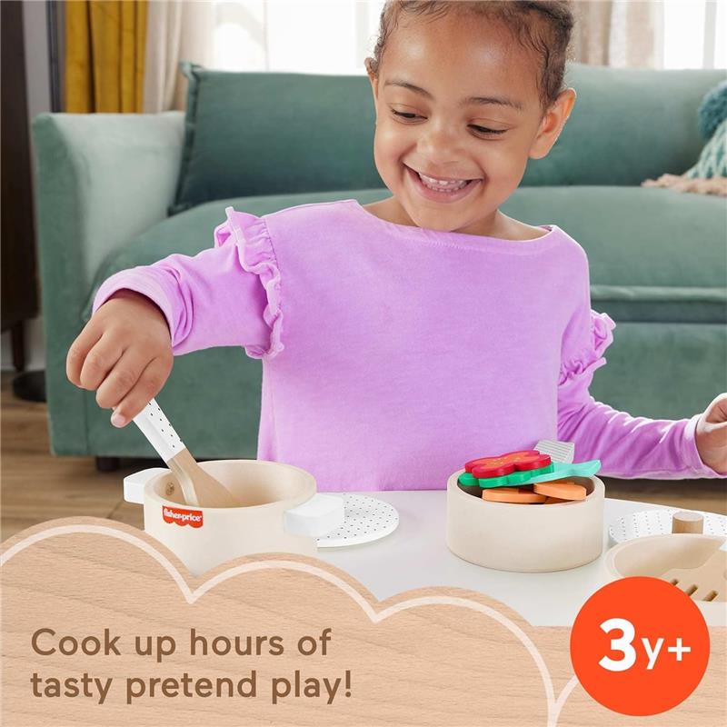 Child in a lavender shirt joyfully pretends to cook with a Fisher Price wooden pots and pans set, mixing colorful food items.
