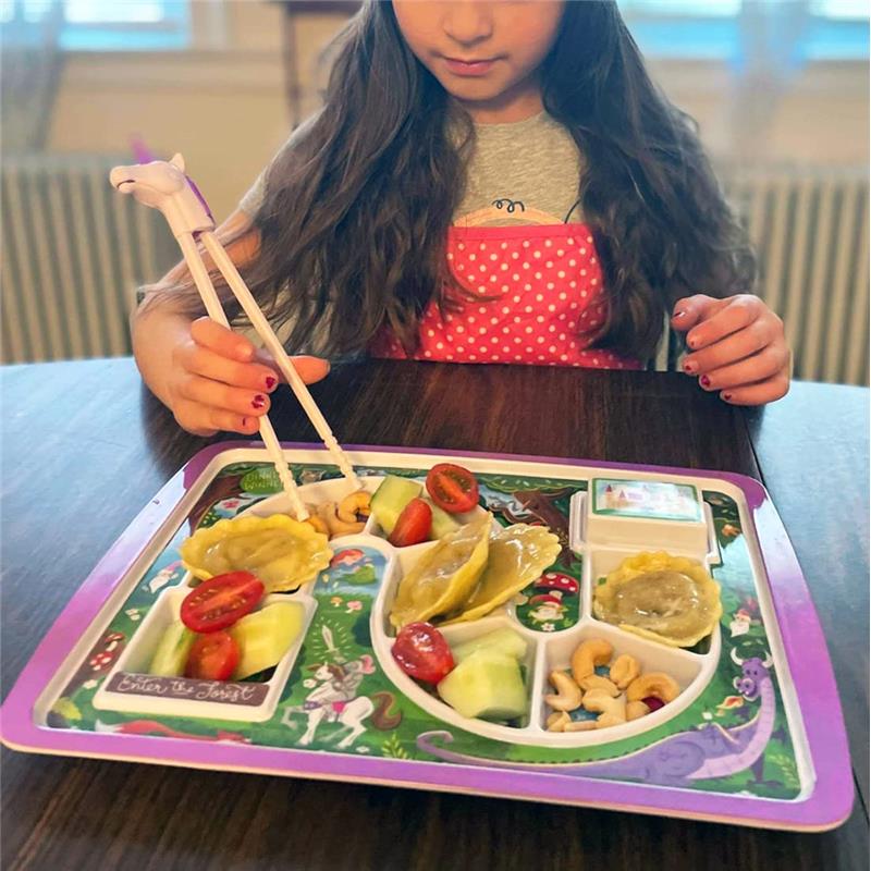 Child using chopsticks to eat from a colorful, divided plate featuring various foods like dumplings, cucumbers, and cherry tomatoes.