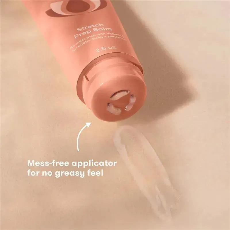 Frida Mom Stretch Prep Balm in a peach-colored tube with a mess-free applicator, with balm visible on a surface.
