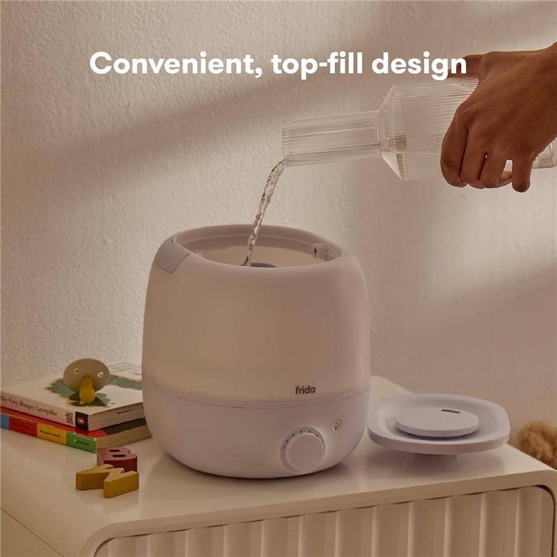 A person pours water into a Fridababy 3-in-1 Cool Mist Humidifier, featuring a top-fill design and adjustable settings.