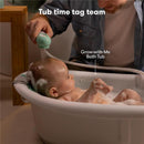 Fridababy Control The Flow bathtub sprayer attachment is used by an adult to rinse a baby in a bubble-filled tub.