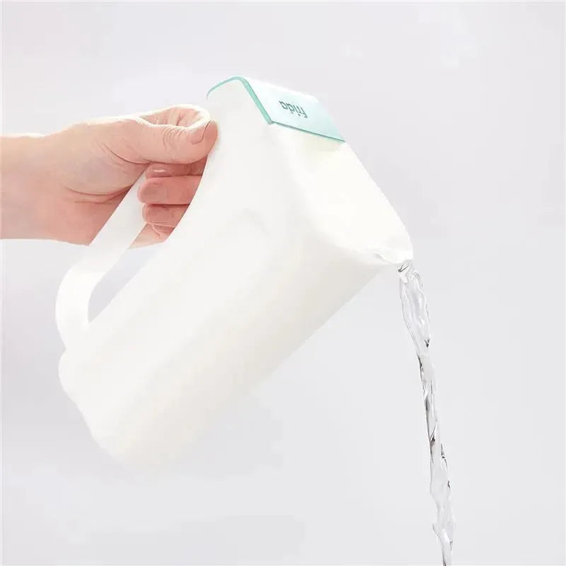 Fridababy Control The Flow Rinser being poured, showcasing a hand holding the white container with water flowing from the spout.