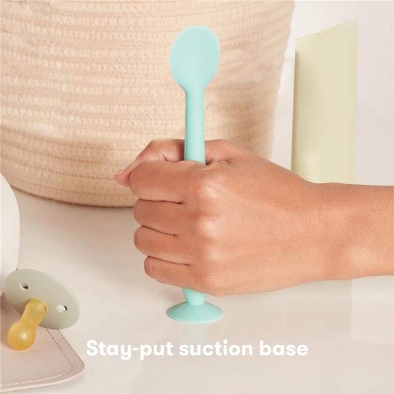 Diaper Cream Booty Brush by Fridababy, held in a hand, features a mint green silicone brush head with a suction base.