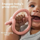 Muted pink FridaBaby Get-A-Grip Teether being held by a baby, engaging their grasp reflex, with text highlighting its design features.