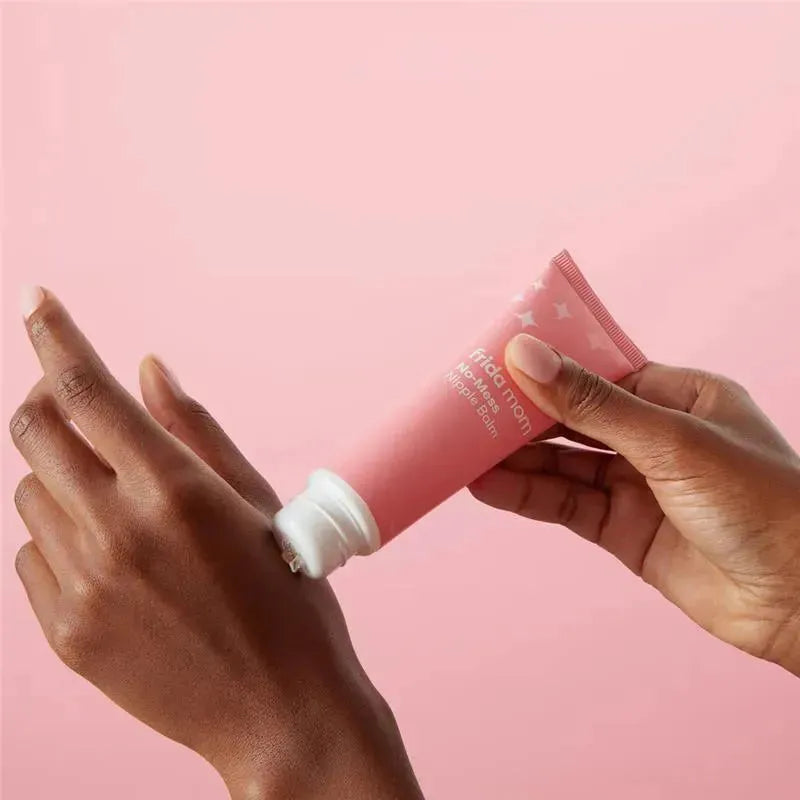 Frida Mom No-Mess Nipple Cream tube being applied to a hand, featuring a pink background.