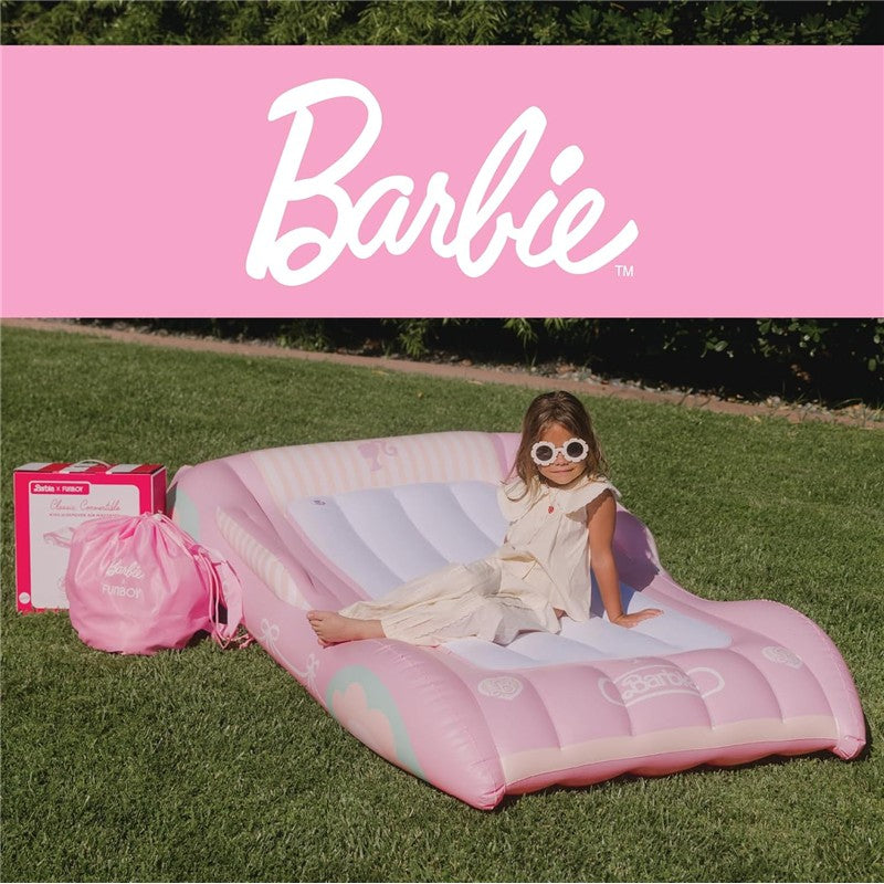 Kids air mattress in pink with Barbie branding, featuring a girl sitting on it, surrounded by outdoor grass.
