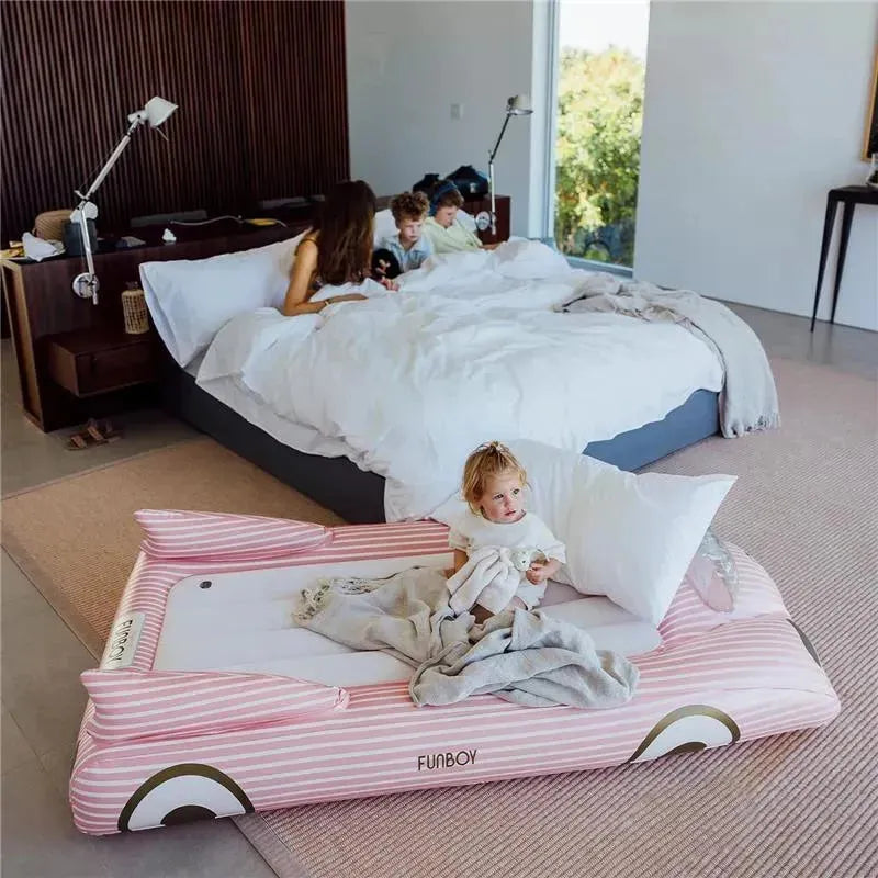 Kids pink inflatable travel bed with a child sitting on it, fluffy pillows, and cozy blankets in a stylish bedroom.