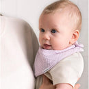 Baby girl wearing a light purple bandana bib, held by an adult, with a soft expression and bright blue eyes.