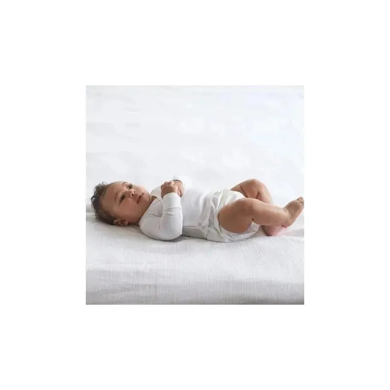 Long-sleeve white side-snap shirt being worn by a baby lying on a light-colored textured surface.