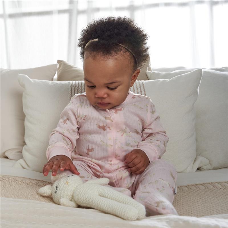 Toddler in a pink 2-way zip sleep suit playing with a light-colored toy bunny on a cozy chair.