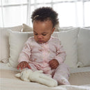 Toddler in a pink 2-way zip sleep suit playing with a light-colored toy bunny on a cozy chair.