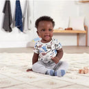Baby boy sitting on a rug, wearing a short sleeve onesie with a multicolor dinosaur print and gray pants.