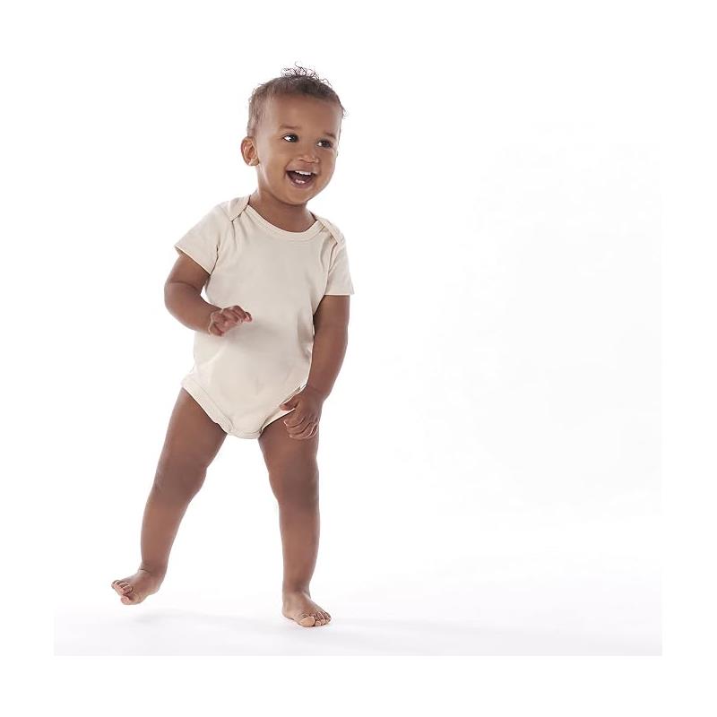 Toddler wearing a light beige Gerbe onesie, smiling and standing on bare feet with a playful pose.