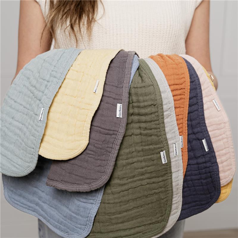 Assorted muslin burp cloths in various colors held by a person, showcasing soft, textured fabric and brand labels.