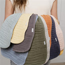 Assorted muslin burp cloths in various colors held by a person, showcasing soft, textured fabric and brand labels.