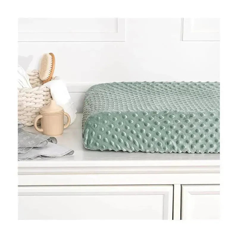 Green changing pad cover with a textured surface, placed on a white surface alongside baby care items.