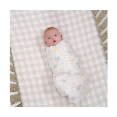 Gerber Bedding muslin blanket in a crib, wrapping a baby, featuring a neutral celestial pattern of stars and moons.