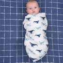 Muslin blanket swaddled around a baby, featuring a whale pattern, resting on a grid-patterned blue background.