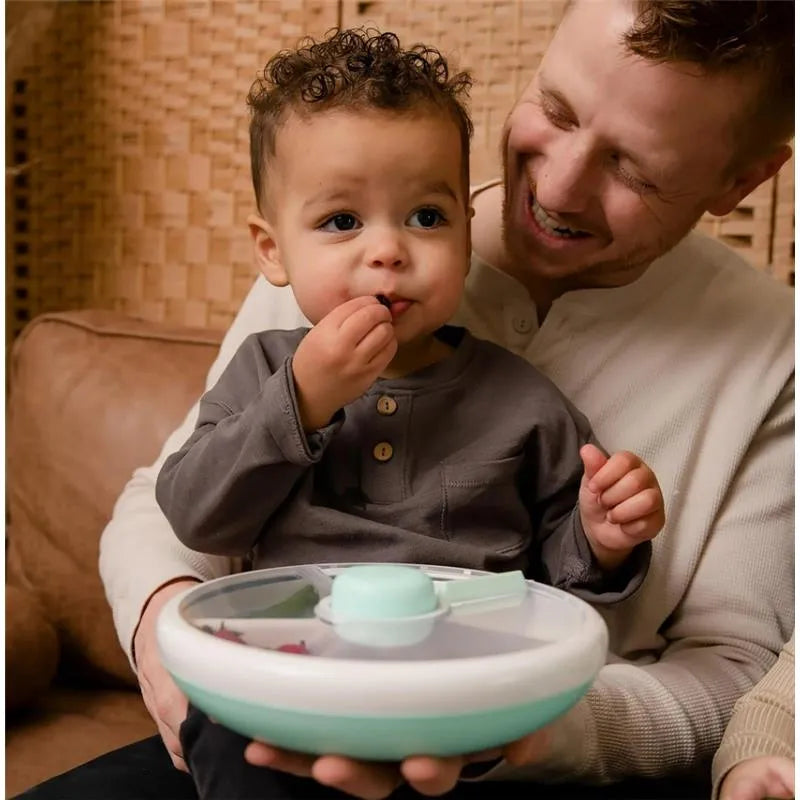 Child holding a Gobe Kids Large Snack Spinner in Macaron Blue, smiling while eating a snack with a parent nearby.
