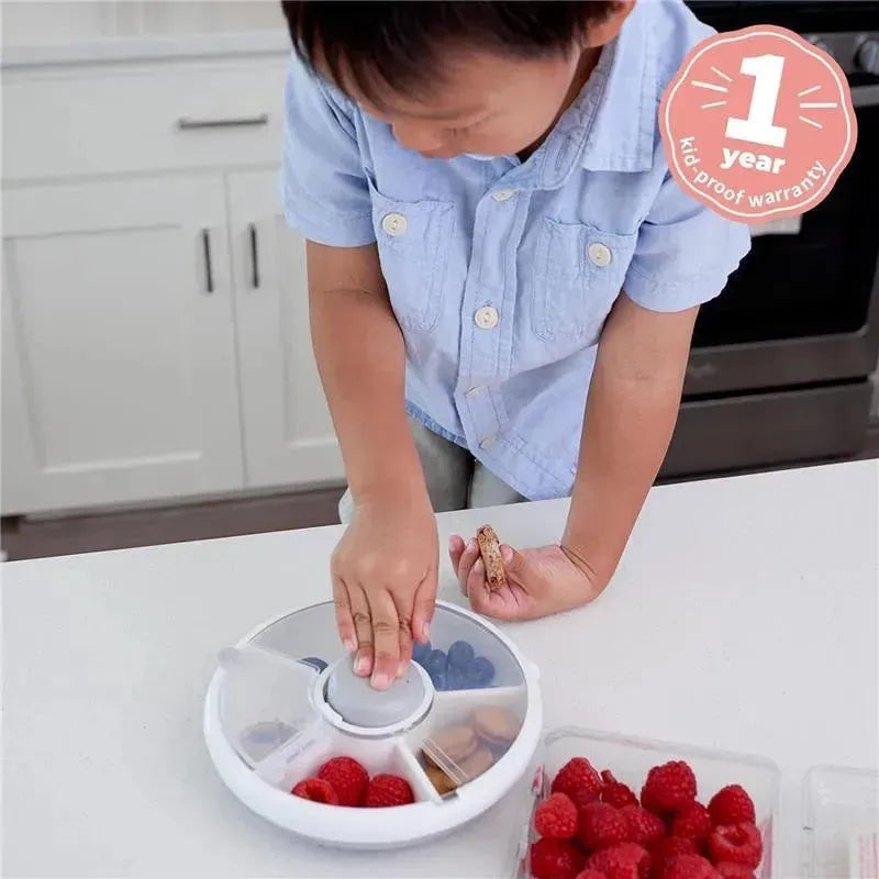 Boy in a blue shirt using the GoBe Kids Snack Spinner, filled with raspberries and blueberries, on a countertop.