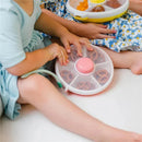 Kids using the GoBe snack spinner with hand strap, featuring pretzels and colorful snacks in sections.