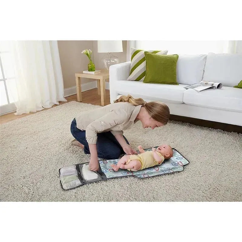 A woman smiles at a baby on a colorful changing pad, interacting warmly in a well-lit living room.