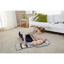 A woman smiles at a baby on a colorful changing pad, interacting warmly in a well-lit living room.