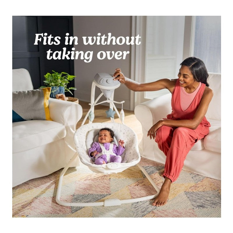 Graco Simple Sway Portable Baby Swing with a smiling infant in a purple outfit, a woman adjusting the swing, and plants in a cozy living room.