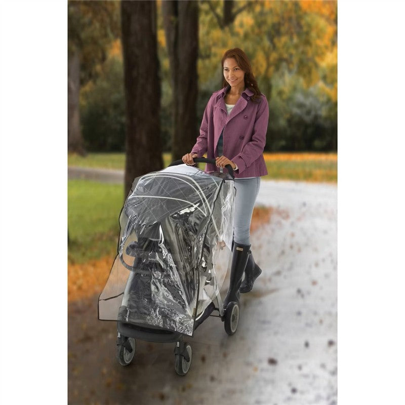 Woman in a purple jacket walking with a Graco Travel System stroller covered by a clear weather shield on a path.