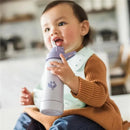 Toddler holding a Sage Green Sprouts 10 Oz Sprout Ware Straw Bottle, smiling while drinking from the straw.
