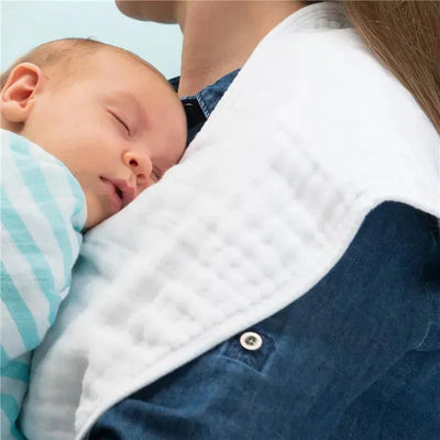 Organic muslin burp cloth draped over a person holding a sleeping baby in a striped blanket.