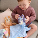 Child playing with Gund Bingo Lovey Plush, holding a blue and white plush with a happy face, surrounded by other soft toys.