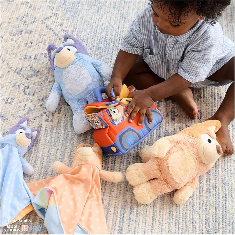 A child plays with a Gund Bingo Plush toy, surrounded by colorful plush animals and a toy vehicle on a soft rug.