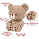 Plush beige teddy bear with oversized head, short arms, and extra-large squishy feet featuring faux suede paw pads and heart stitching.