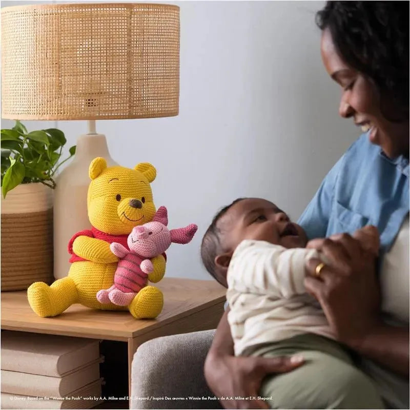 Knit Winnie the Pooh holding Piglet next to a woman smiling at a baby in a cozy room setting.