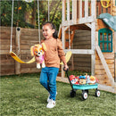 Girl joyfully carries a plush dog toy while pulling a wagon filled with colorful character plush toys in a backyard.