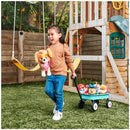 Girl smiling and holding a Plush PAW Patrol Zuma toy, pulling a wagon with other plush characters in a playground.