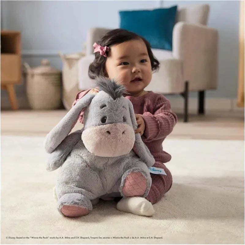 A toddler smiles while hugging a soft, plush Eeyore toy, showcasing the Gund Oh So Snuggly Eeyore product.