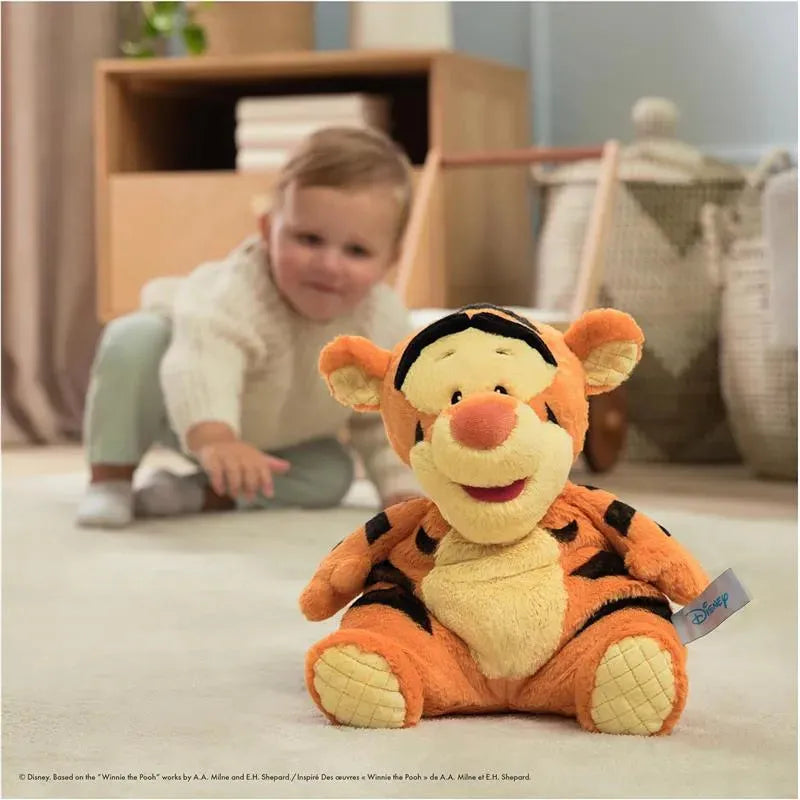 Gund Oh So Snuggly Tigger plush toy sits in a bright room, with a young child reaching towards it in the background.