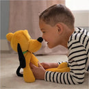 A boy in a striped shirt smiles at a yellow plush toy dog, Gund - Pluto 15, while sitting on a soft carpet.
