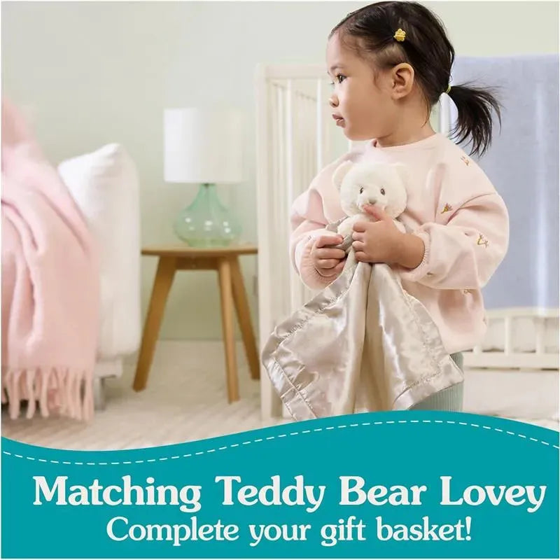 Toddler holding a Gund Spiritual Bear Lovey blanket and stuffed bear, wearing a pink sweater in a cozy bedroom setting.