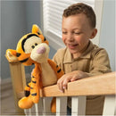 A smiling child holds a plush Tigger toy, showcasing its orange and black stripes, near a wooden railing.