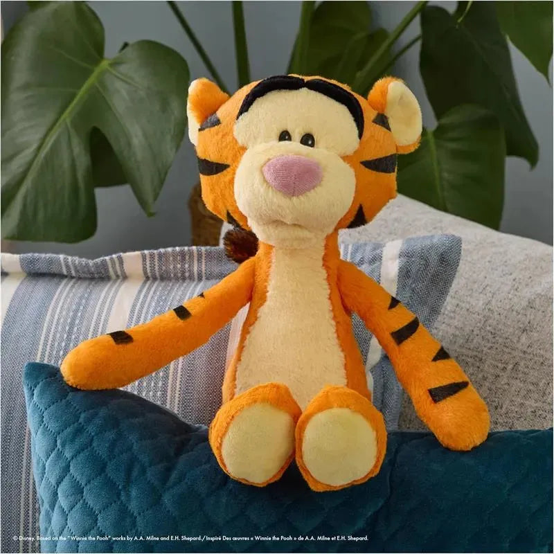 Gund Tigger plush toy, orange with black stripes, sitting on a blue pillow among cushions and greenery.