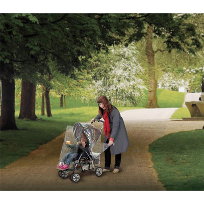 Woman pushing a stroller with a weather shield in a park, with a child seated inside.